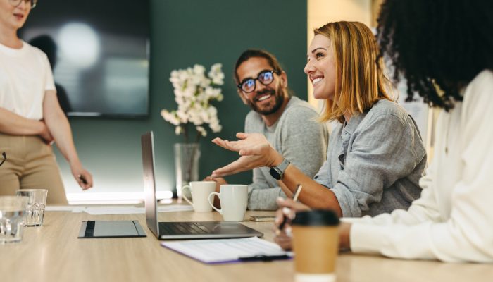 Business woman talking to her colleagues during a meeting in a boardroom. Group of happy business people working together in a creative office.